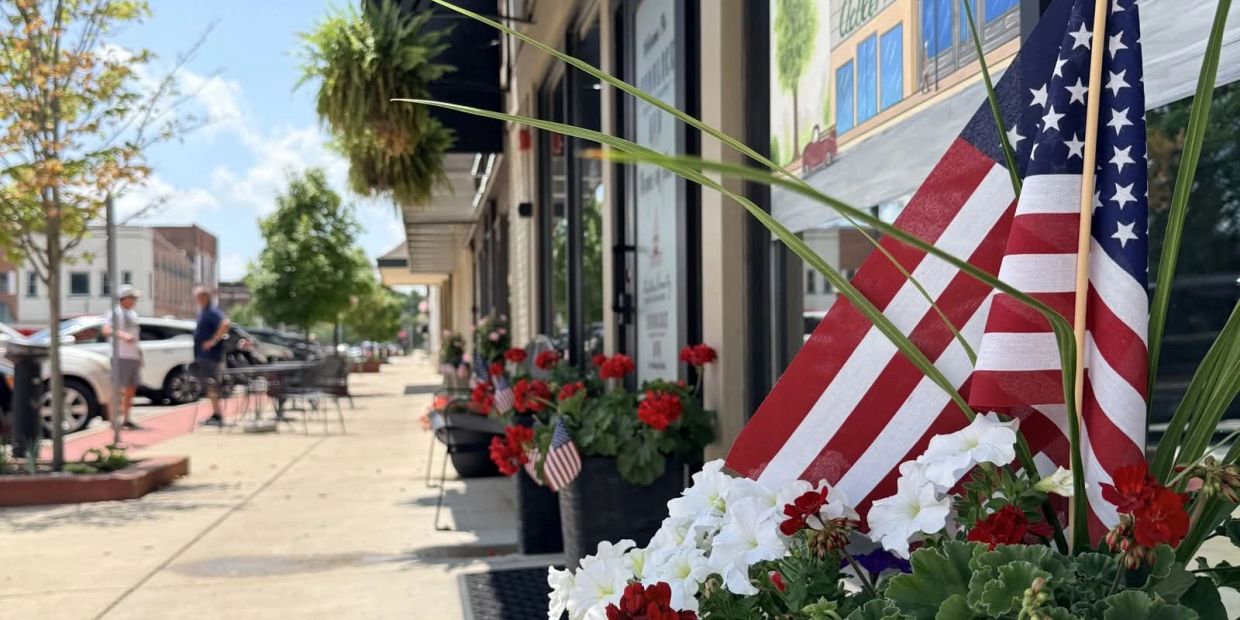 American flags and flowers outside a downtown shop on a sunny day.