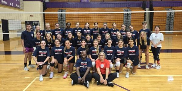 Volleyball team posing in gym wearing matching shirts.