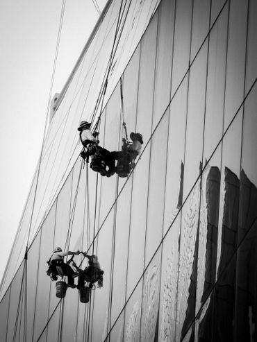 Two workers cleaning a glass building while suspended by ropes.