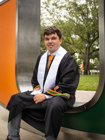Young man in graduation gown sitting in a colorful outdoor sculpture.
