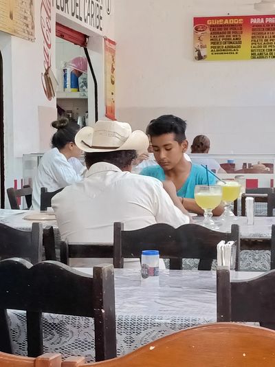 Two men eating, drinking, and conversing in Latin America.
