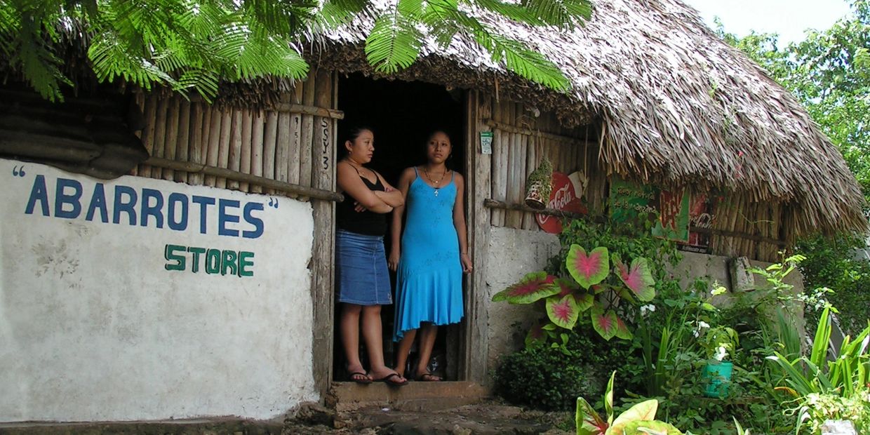 Two young Maya women look out from the doorway of their rustic store.