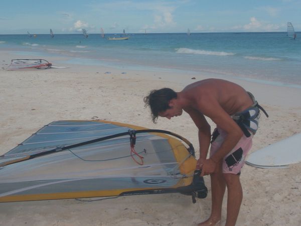 Guide adjusting a windsurfing rig on the beach.