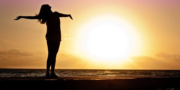 Silhouette of a person with arms outstretched at sunset by the sea.