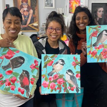 Three women holding bird paintings and smiling.
