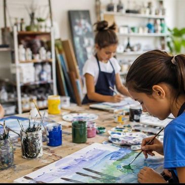 Two girls painting in a studio with focus on one painting a landscape.