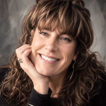 Smiling woman with curly hair resting her chin on her hand.