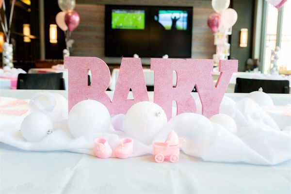 Pink baby shower decorations with letters, balloons, and tiny baby items.