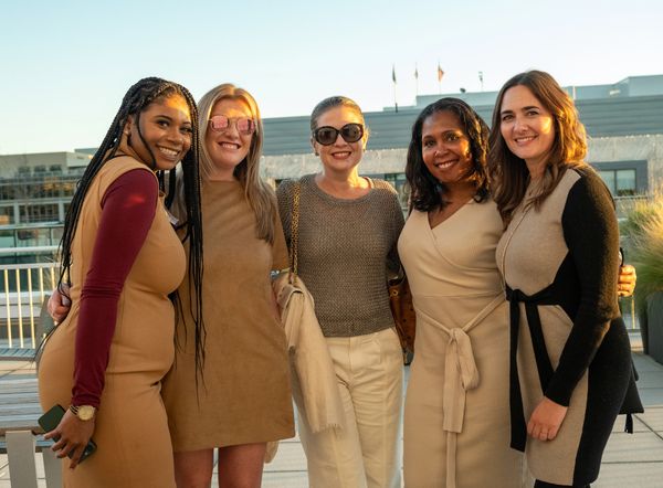 Five diverse women smiling together outdoors at sunset.