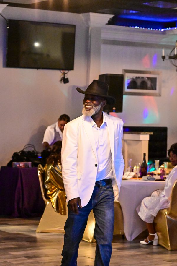 Man in white blazer and black hat smiling at a party.