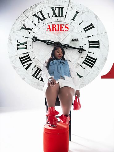 Woman sitting on a chair in front of a large clock with Aries text.