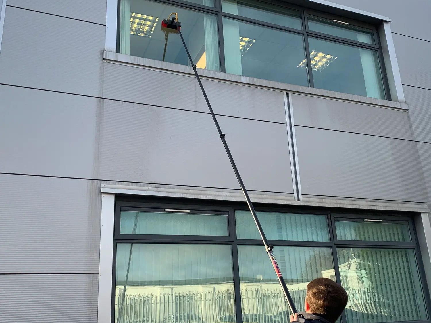A person cleaning exterior windows using a water fed brush