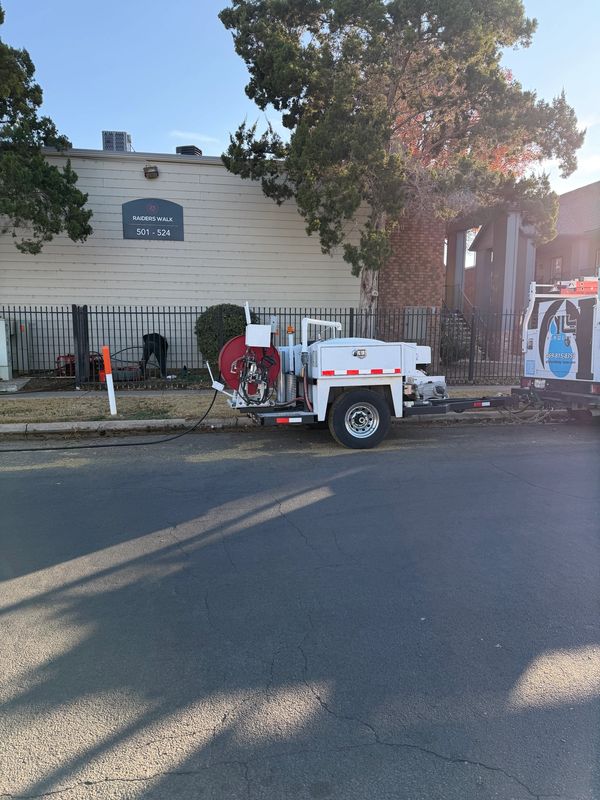 A white utility trailer parked on the street beside a residential building.
