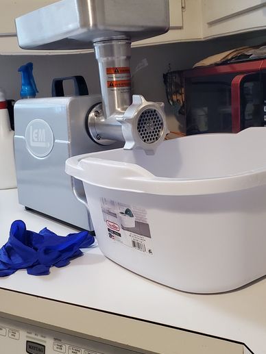 Meat grinder machine on kitchen counter with basin and gloves.