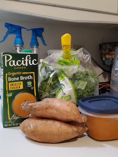 Sweet potatoes, bone broth, and greens on a kitchen counter.