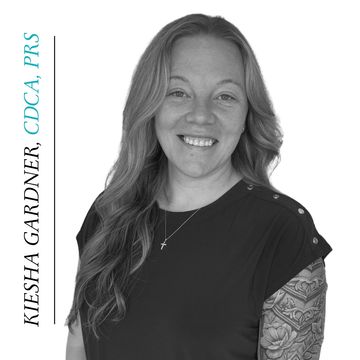 Black and white portrait of a smiling woman with long hair and a tattooed arm.