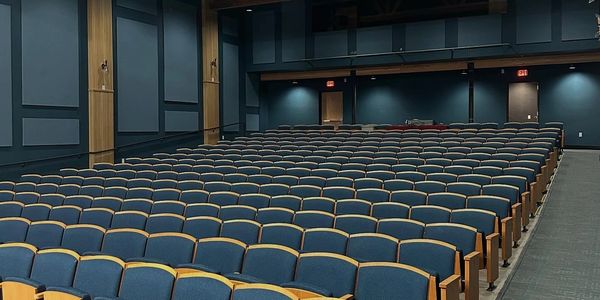 Empty auditorium with rows of blue seats and wood accents.