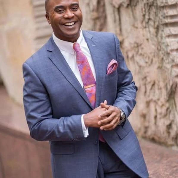 Man in a blue suit smiling warmly outdoors.
