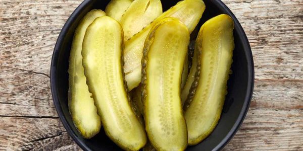 A bowl of sliced pickles on a wooden surface.