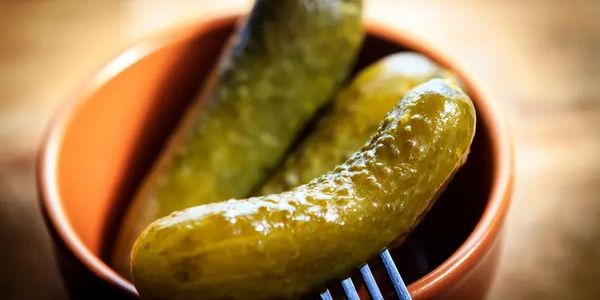 Pickles in a bowl, one on a fork.