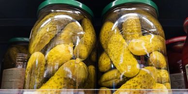 Jars filled with pickled cucumbers on a store shelf.
