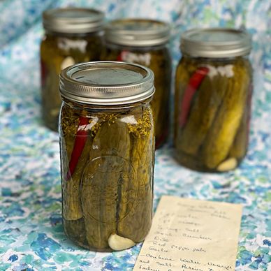 Jars of homemade pickles with spices and garlic on a floral cloth.