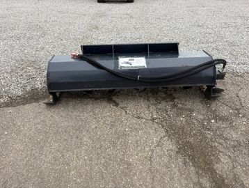 A gray industrial sweeper attachment on cracked pavement.