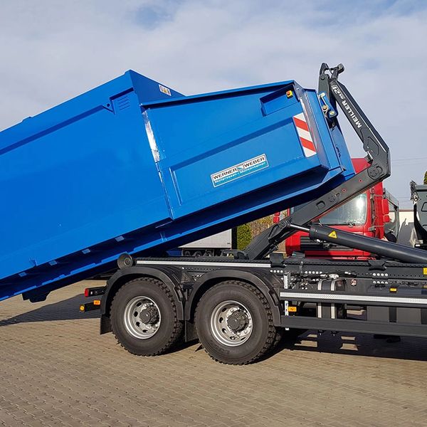 Blue container being loaded onto a truck chassis outdoors.