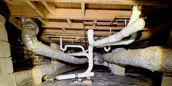 Insulated HVAC ducts and white PVC plumbing pipes in a basement crawl space.