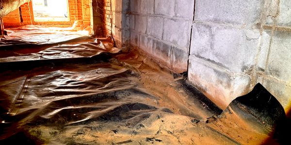 A damp, dirty crawl space with plastic sheeting and concrete block walls.