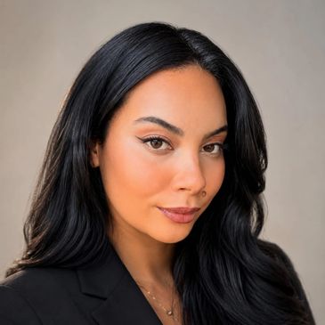 Confident woman with sleek black hair and natural makeup poses in professional attire.