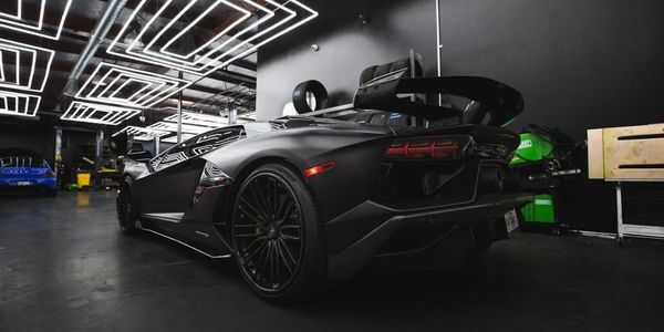Matte black luxury sports car in a modern, well-lit garage.