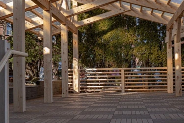 A wooden pergola with transparent roofing and tiled floor in an urban setting.