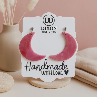 Pink crescent moon earrings displayed on a handmade jewelry card.