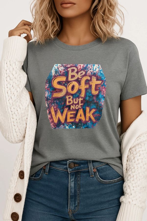 Woman wearing a gray t-shirt with colorful text: 'Be Soft But Not Weak'.