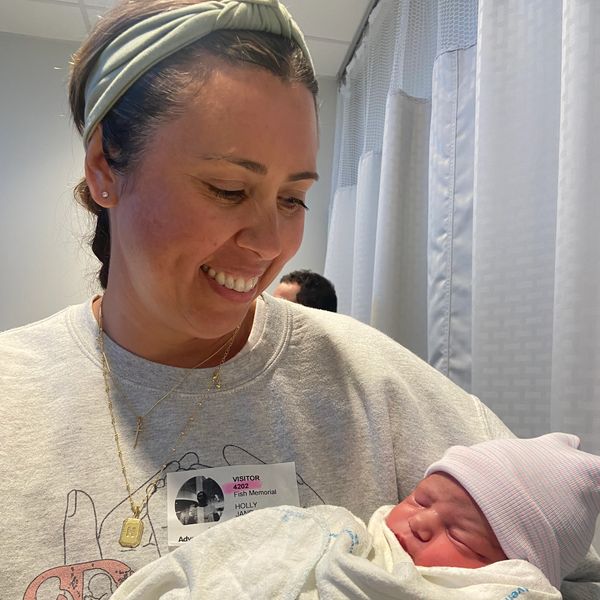 Woman smiling and holding a newborn baby wrapped in a blanket.