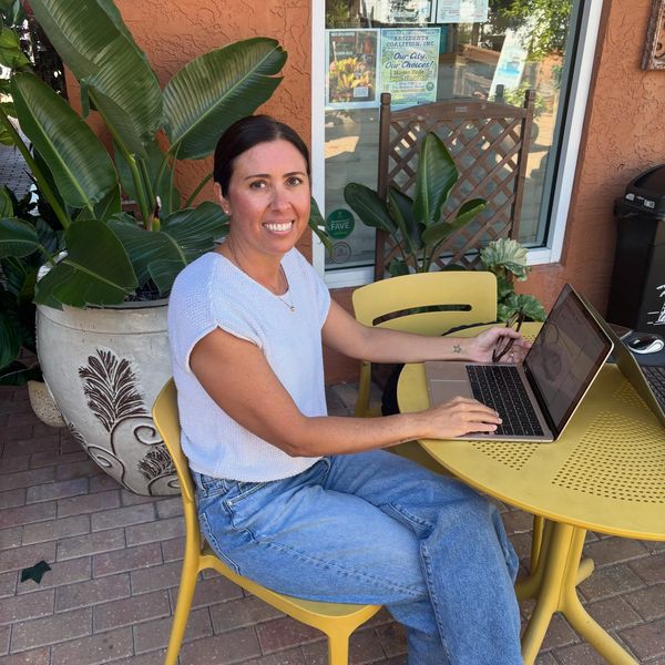 Woman sitting outside using a laptop at a yellow table.