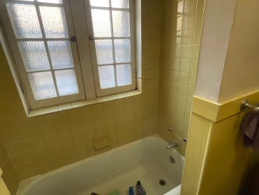 A yellow-tiled bathroom with a white bathtub and a frosted window.
