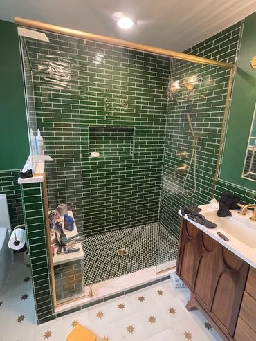 Modern bathroom shower with green subway tiles and gold fixtures.