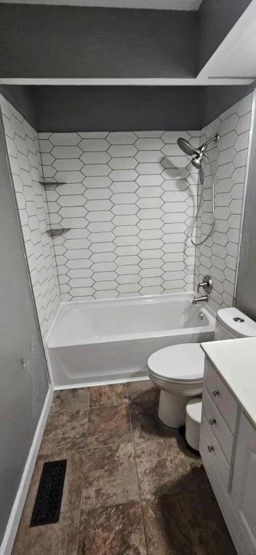 Modern bathroom with white hexagonal tile shower, bathtub, toilet, and vanity.