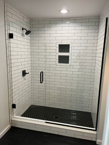 Modern glass shower with white subway tiles and black hexagonal floor tiles.