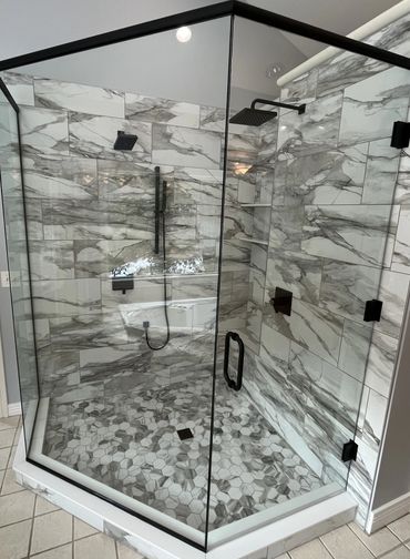 Modern glass shower with marble tile walls and hexagonal floor tiles.