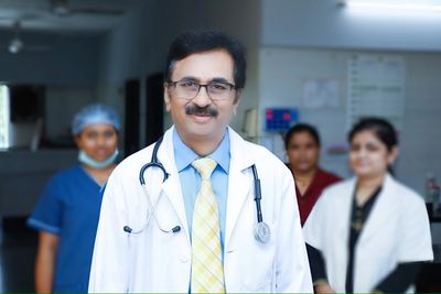 Smiling doctor in a white coat with a stethoscope, accompanied by medical staff in a hospital setting.
