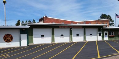 Exterior of a fire station with four garage doors and a fire department emblem.