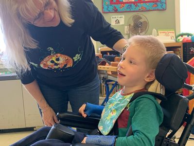Woman standing next to a boy in a wheelchair. Both are smiling