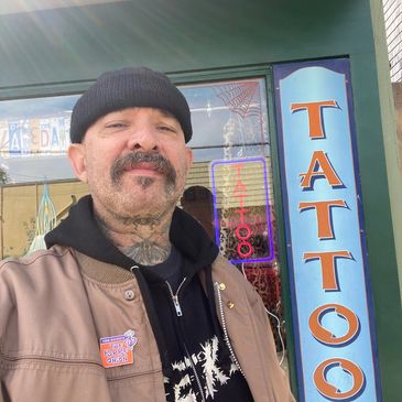 Man with tattoos standing outside a tattoo shop.