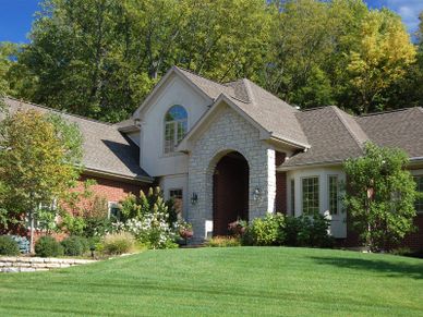 Elegant brick house with stone archway and lush green lawn.