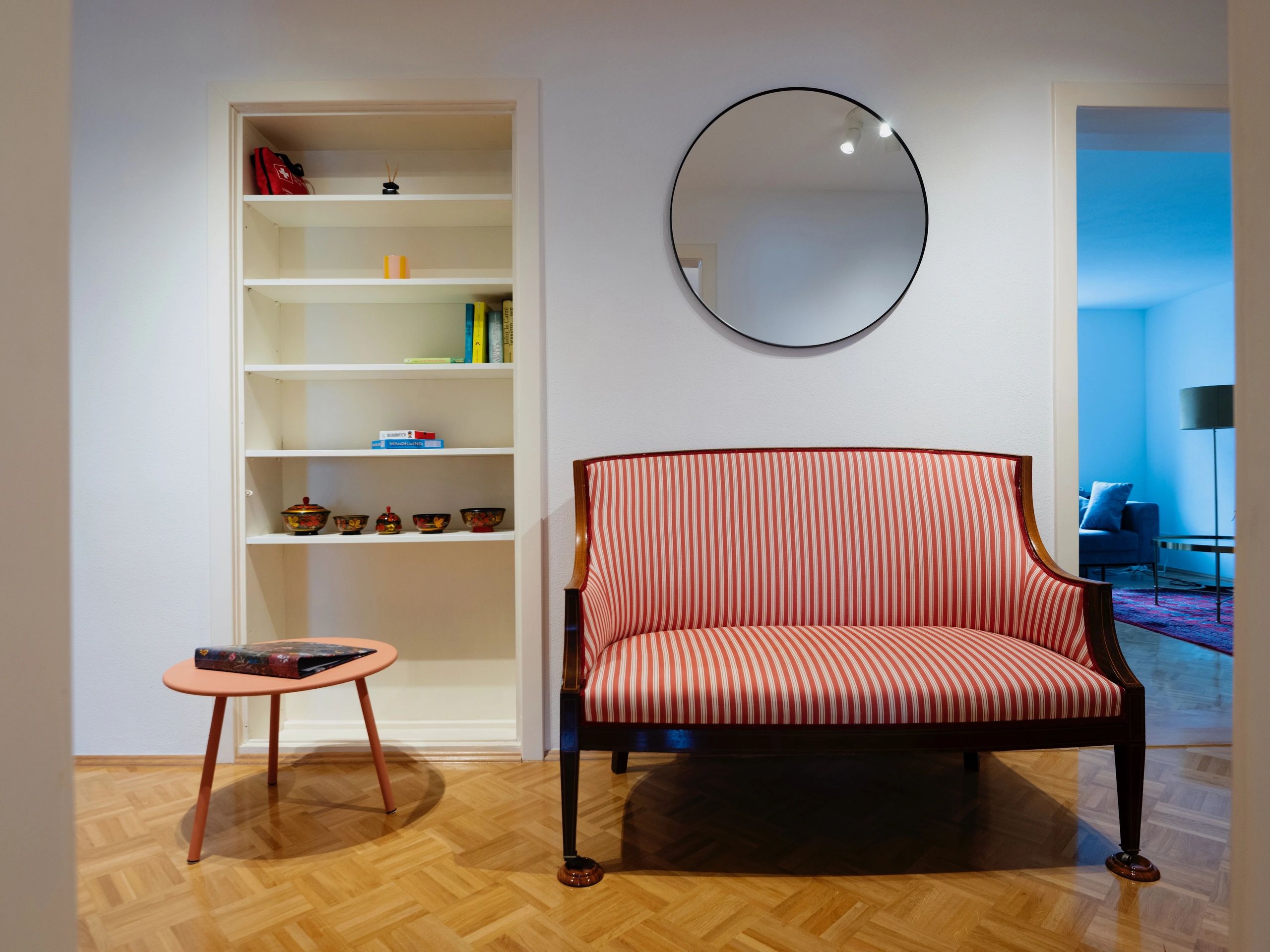 Cozy room with a striped sofa, round mirror, and built-in shelves.
