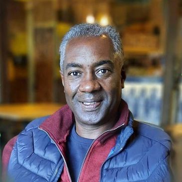 Smiling man wearing a blue vest and red sweater indoors.