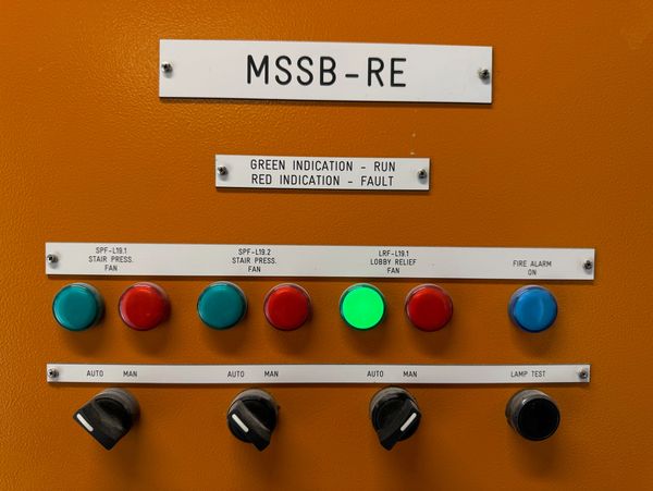 Control panel with colored buttons and switches indicating fan status and fire alarm.